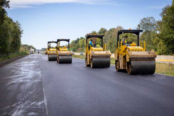 four road rollers staggered in line smoothing out asphalt